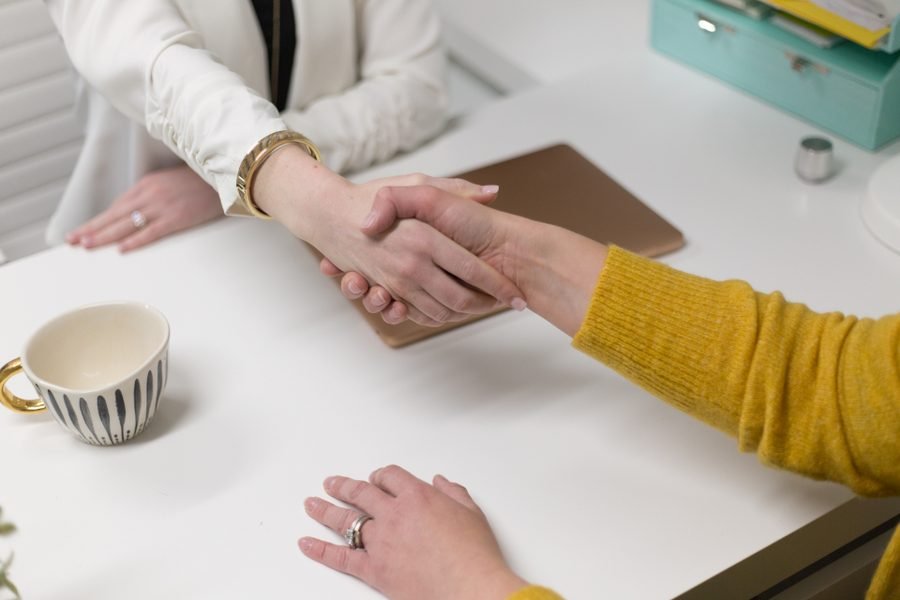 Two people shaking hands across a desk after agreeing terms